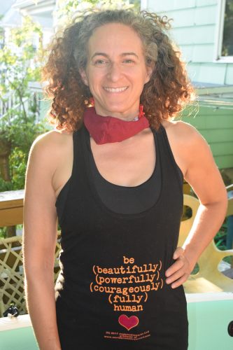 Happy customer, Julia, wearing the "be (beautifully) (powerfully) (courageously) (fully) human" tank top design with the heart under the text, also sporting a warm smile, her pandemic mask off for a moment.